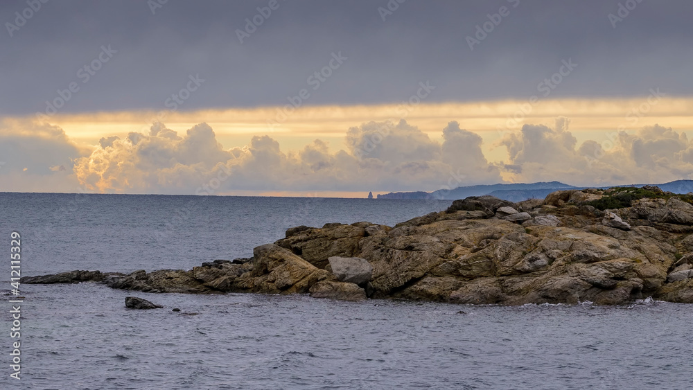 Paisaje relajante de la costa rocosa del norte de la Costa Brava en la bahía de Rosas, Alt Emporda, Cataluña, España con un cielo de nubes de tormenta al fondo y luz del sol al atardecer
