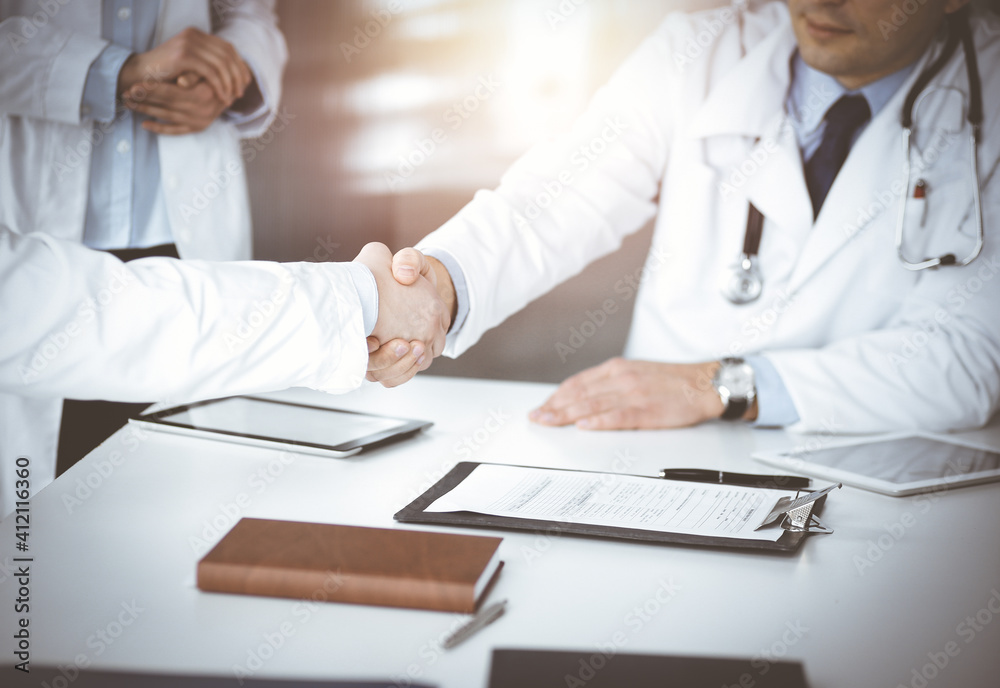 Unknown doctors are shaking their hands as agreement about patient's diagnosis, close-up. Perfect medical help, insurance in health care, medicine concept