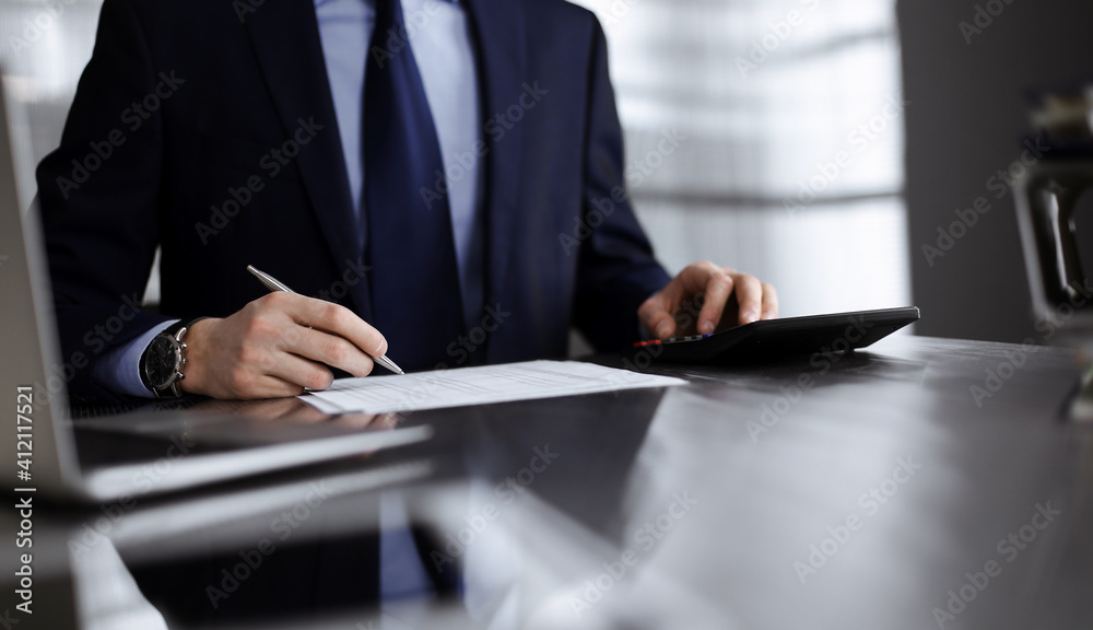 Unknown man accountant in blue blazer use calculator and computer with holding pen on while staying at home during covid pandemic. Taxes and audit concept Unknown man accountant in blue blazer use calculator and computer with holding pen on while staying at home during covid pandemic. Taxes and audit concept
