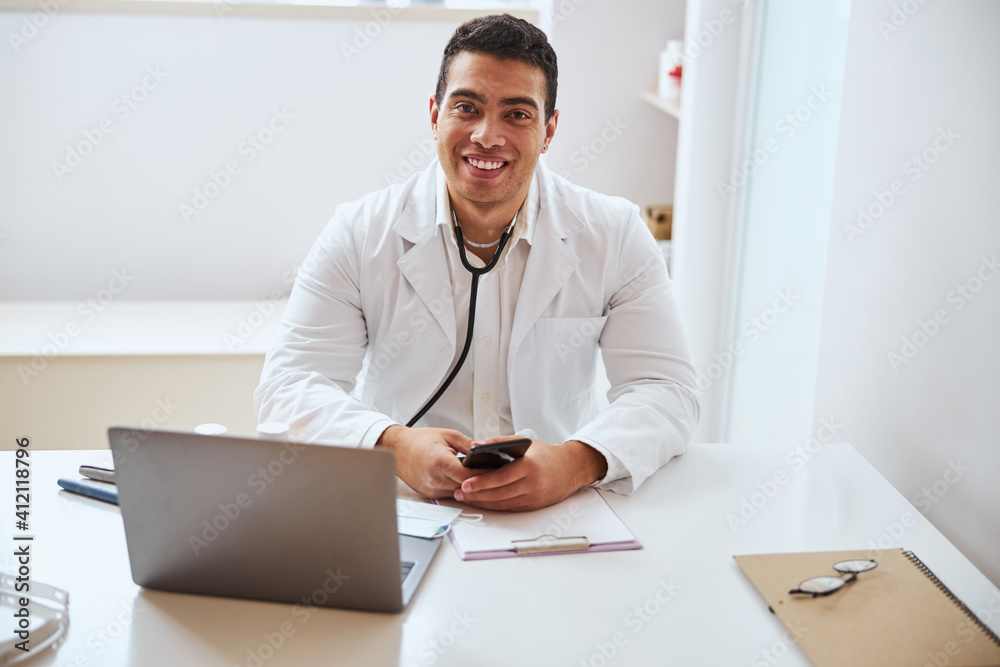 Fototapeta premium Handsome confident man in white robe holding mobile phone in arms