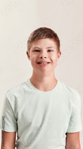Portrait of cheerful disabled boy with Down syndrome smiling at camera while posing isolated over white background
