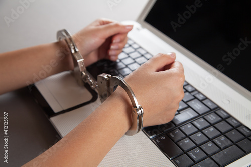 Hands and handcuffs on laptop keyboard. Cyber Crime.