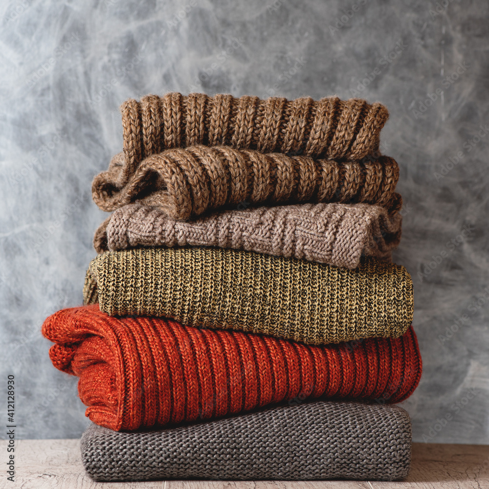 Stack of folded knitted warm wool women sweaters and scarfs on gray background. Season of warm clothes. Fashion concept.