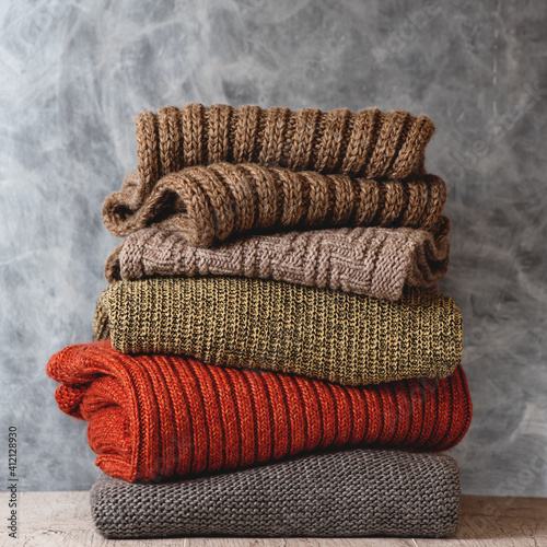 Obraz na płótnie Stack of folded knitted warm wool women sweaters and scarfs on gray background. Season of warm clothes. Fashion concept. w salonie