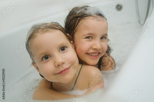 Children's hygiene. Two lovely children bathe together in the bathroom. Playful girls look out of the bath, smiling looking at the camera. Children's hygiene.
