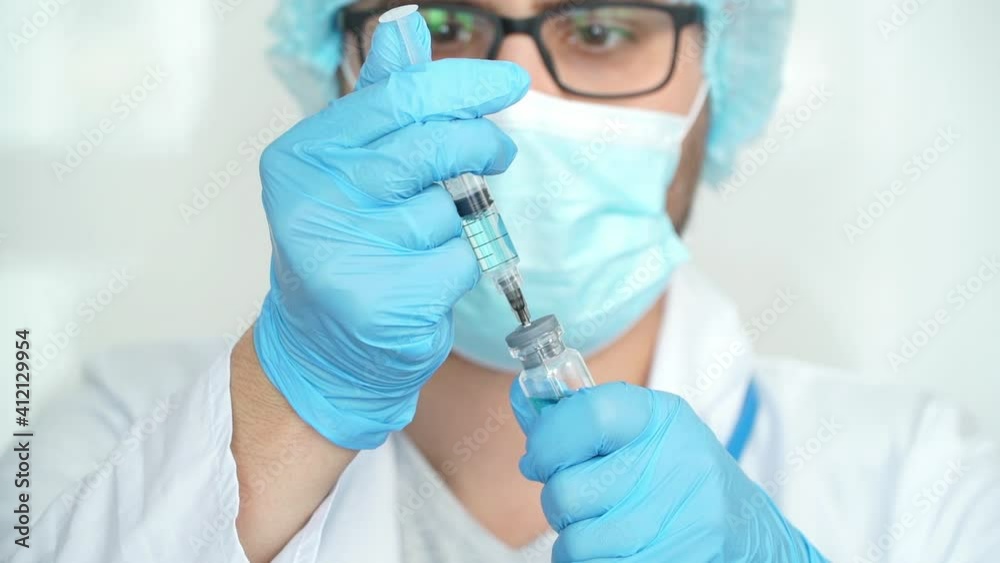 Close up of male doctor in medical gloves, white coat and protective mask fills syringe with drug. Male nurse holds ampoule with vaccine for covid-19. Coronavirus Close up of male doctor in medical gloves, white coat and protective mask fills syringe with drug. Male nurse holds ampoule with vaccine for covid-19. Coronavirus