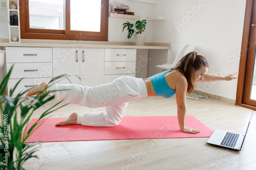 Fit woman doing yoga plank and watching online tutorials on laptop, training in living room or bedroom