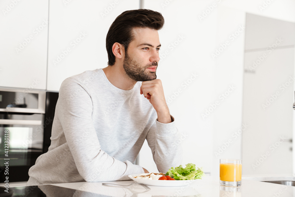 Pleased handsome unshaven man having breakfast at home kitchen Pleased handsome unshaven man having breakfast at home kitchen