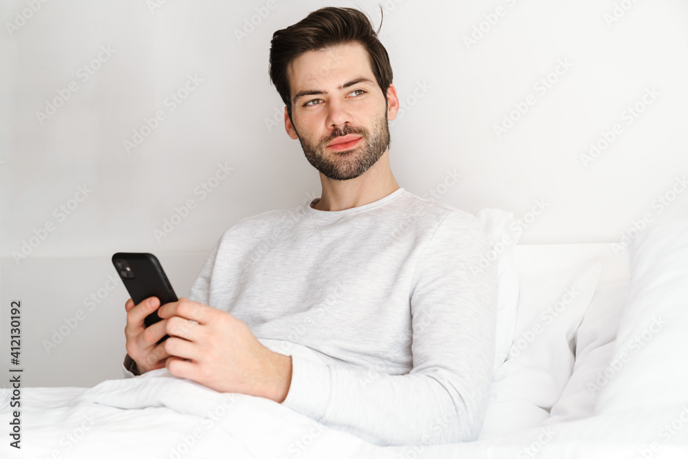 Pleased handsome man using mobile phone while resting in bed Pleased handsome man using mobile phone while resting in bed