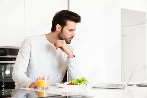 Focused handsome man using laptop while having breakfast