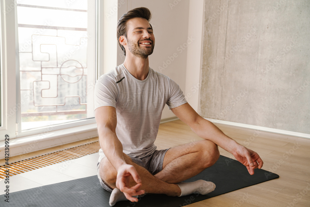 Happy athletic handsome man meditating after workout at home - obrazy, fototapety, plakaty 