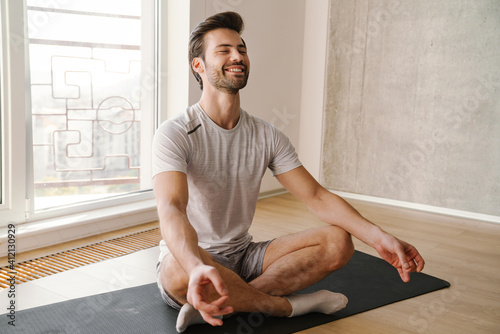 Happy athletic handsome man meditating after workout at home