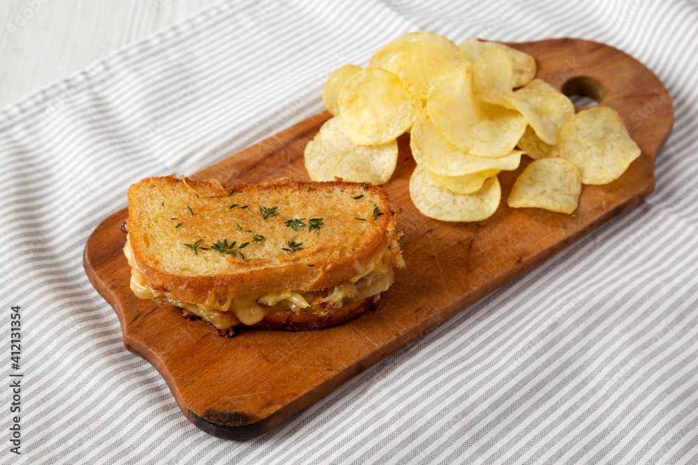 Homemade French Onion Melt Cheese Sandwich with Chips on a rustic wooden board on cloth, side view.