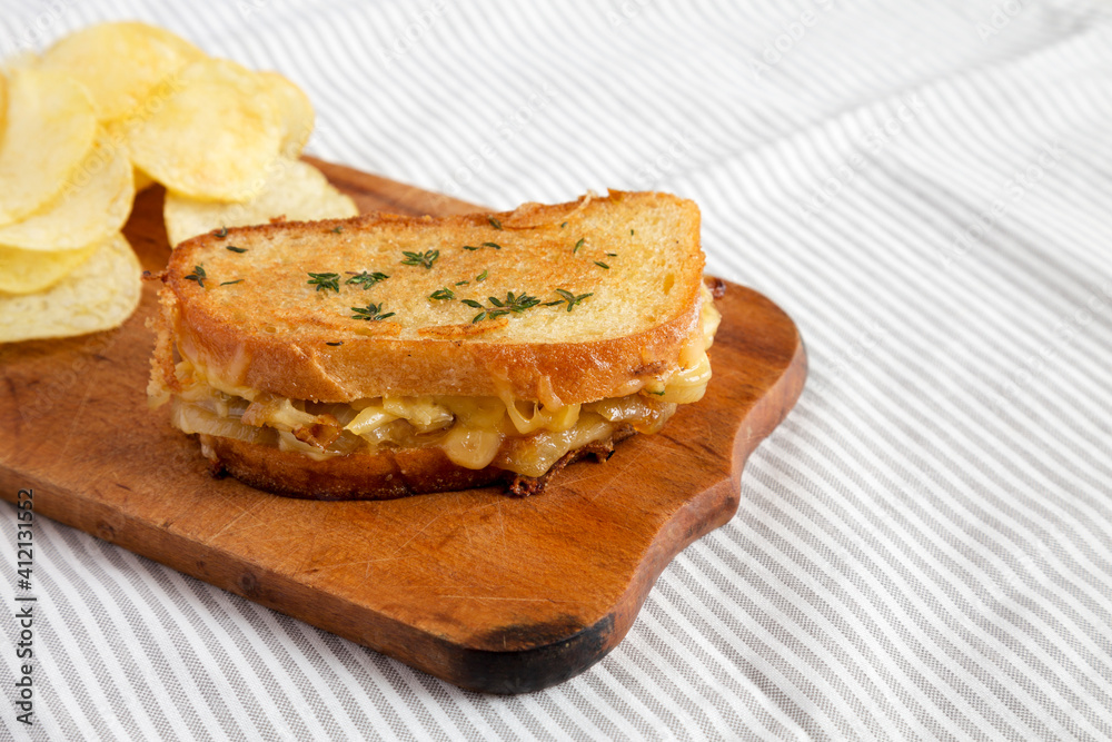 Homemade French Onion Melt Cheese Sandwich with Chips on a rustic wooden board on cloth, low angle view. Copy space. Homemade French Onion Melt Cheese Sandwich with Chips on a rustic wooden board on cloth, low angle view. Copy space.