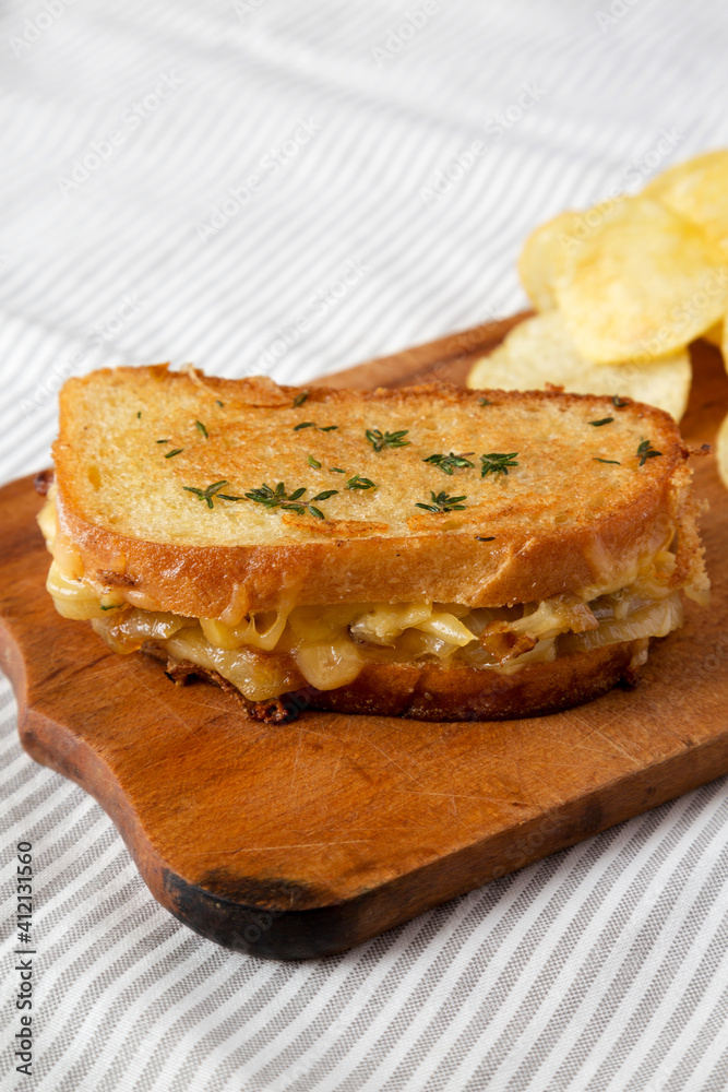 Homemade French Onion Melt Cheese Sandwich with Chips on a rustic wooden board on cloth, low angle view.