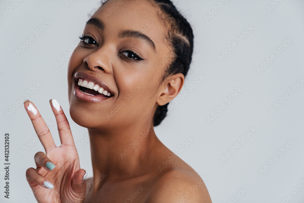 Joyful shirtless african american woman showing face cream Joyful shirtless african american woman showing face cream