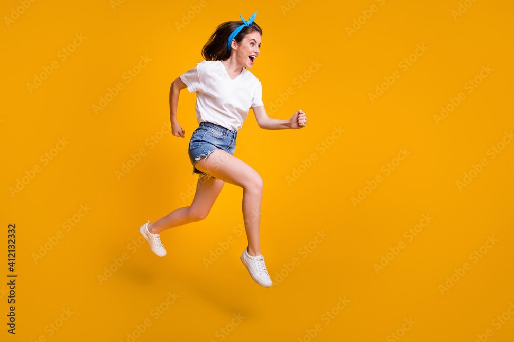Full length body size photo of cheerful young woman running fast jumping high hurrying up on sale isolated on bright yellow color background