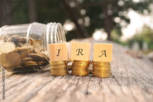 Close up of stacking gold coins and wooden blocks written IRA on nature background and natural lighting. Individual Retirement Account concept