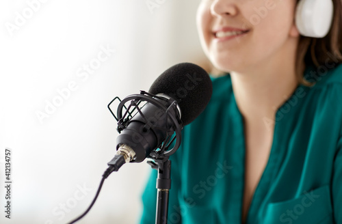 technology, mass media and people concept - close up of woman with microphone and headphones talking and recording podcast at studio