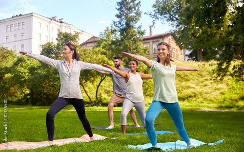 fitness, sport and healthy lifestyle concept - group of happy people doing yoga at summer park
