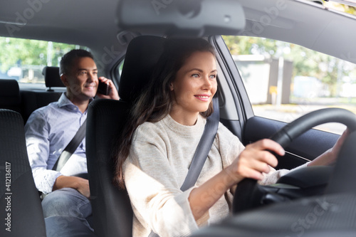 transportation, vehicle and people concept - happy smiling female driver driving car with male passenger calling on phone
