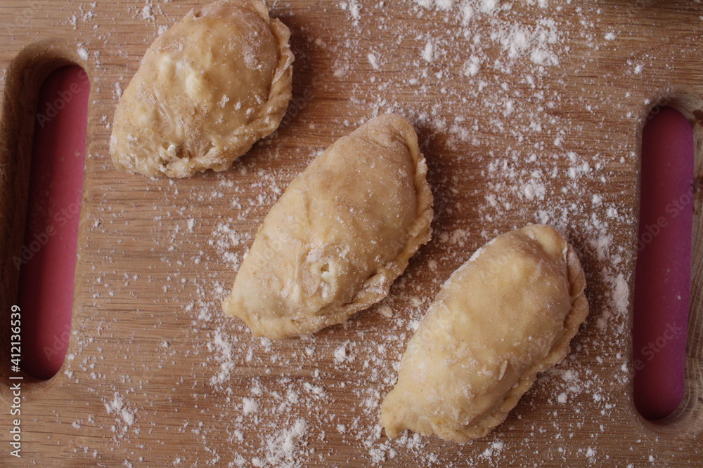 Raw cooking dumplings lie on a board beside egg flour on a pink background view from above Raw cooking dumplings lie on a board beside egg flour on a pink background view from above