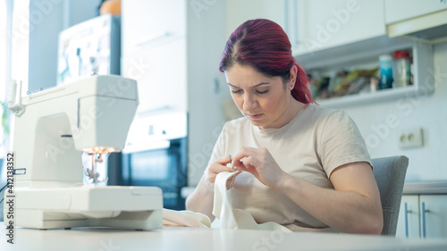 Caucasian woman sews while sitting in the kitchen. Home hobby