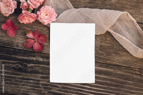 Summer wedding still life scene. Blank greeting card mock-up. Floral composition with pink roses, hydrangea flowers on old wooden table background with silk ribbon. Flat lay, top view.