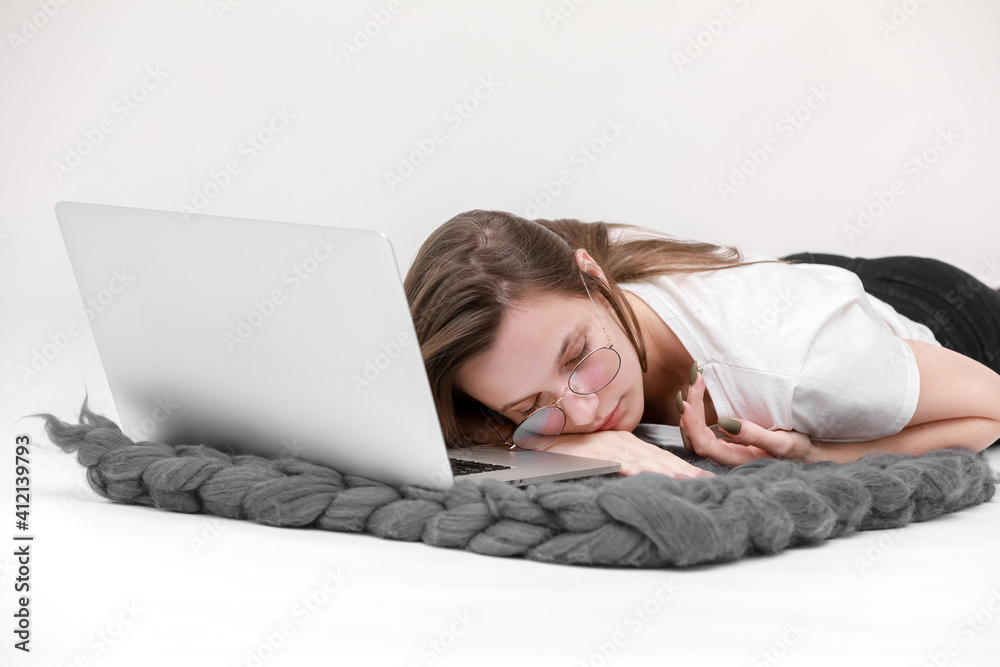 Sleeps in the workplace. Tired young woman working, headache, falling asleep on white background. Learns, using laptop computer on table. Freelance. Writing, typing. Technology concept. Paperwork