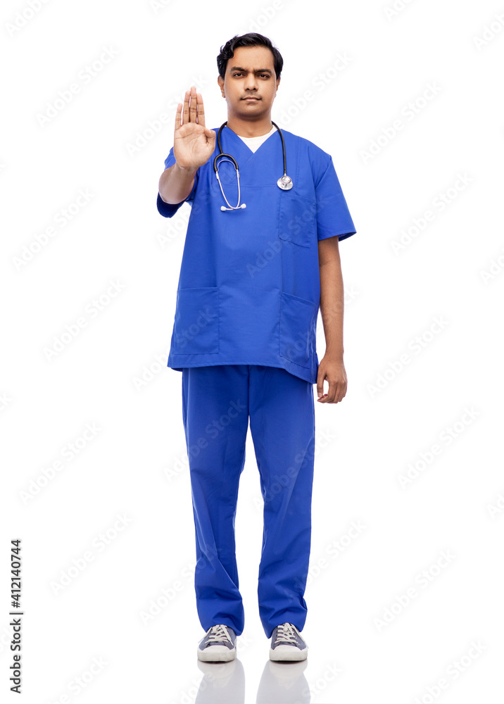 healthcare, profession and medicine concept - indian male doctor in blue uniform showing stop gesture over white background