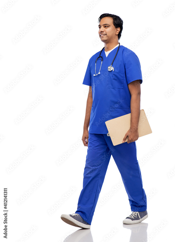 Naklejka premium healthcare, profession and medicine concept - happy smiling indian doctor or male nurse in blue uniform with clipboard and stethoscope walking over white background