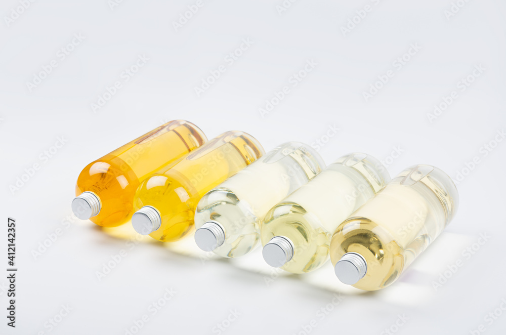 Collection transparent lying bottles with different pale colors liquid, cosmetic product, perfume or drink and silver cap in diadonal row on white background, side view. Collection transparent lying bottles with different pale colors liquid, cosmetic product, perfume or drink and silver cap in diadonal row on white background, side view.