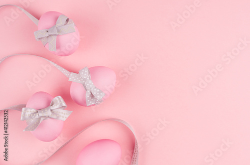 Elegant easter background - eggs with grey bow and wavy ribbons as border on pink pastel color.