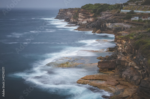 Dramatic coastline views against a moody, stormy sky with whitecaps on a summer day along the Bondi to Bronte coastal walk in Sydney, NSW, Australia.