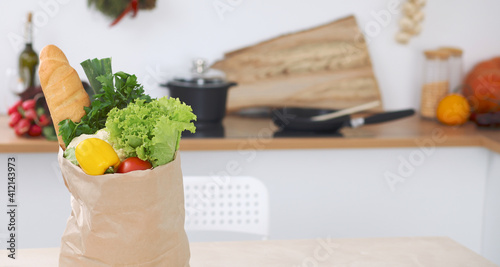 Paper bag full of vegetables on the table in kitchen interiors. Healthy meal and vegetarian concept
