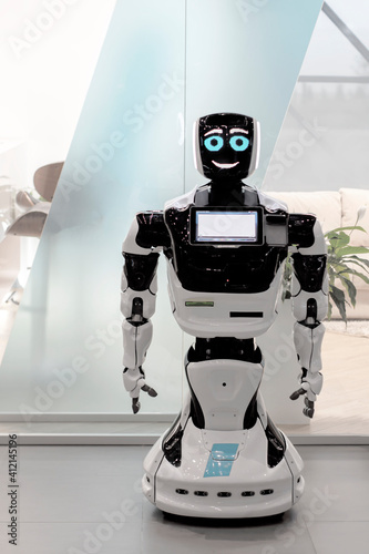 White Robot droid assistant in the office. View from the front. It's a bright room.