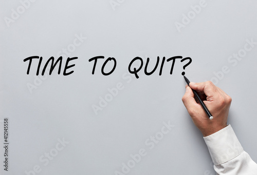 Businessman hand writing the question of time to quit on gray background. Deciding to quit job or to exit business