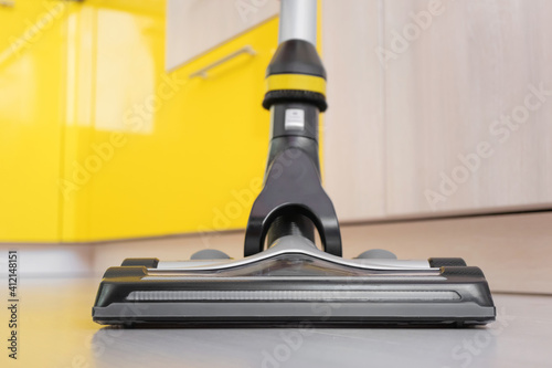 Upright vacuum cleaner brush on the laminate floor close-up. In the background are lockers. Beige, gray and yellow shades. House cleaning concept. photo