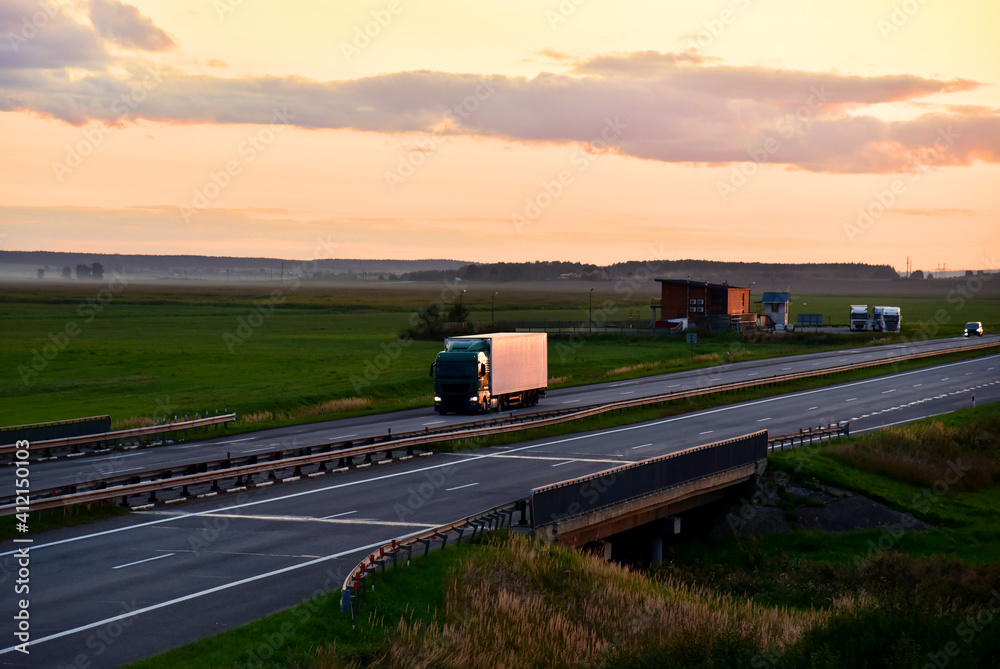 Truck with semi-trailer driving along highway on the sunset background. Goods delivery by roads. Services and Transport logistics. Soft focus. Object in motion.