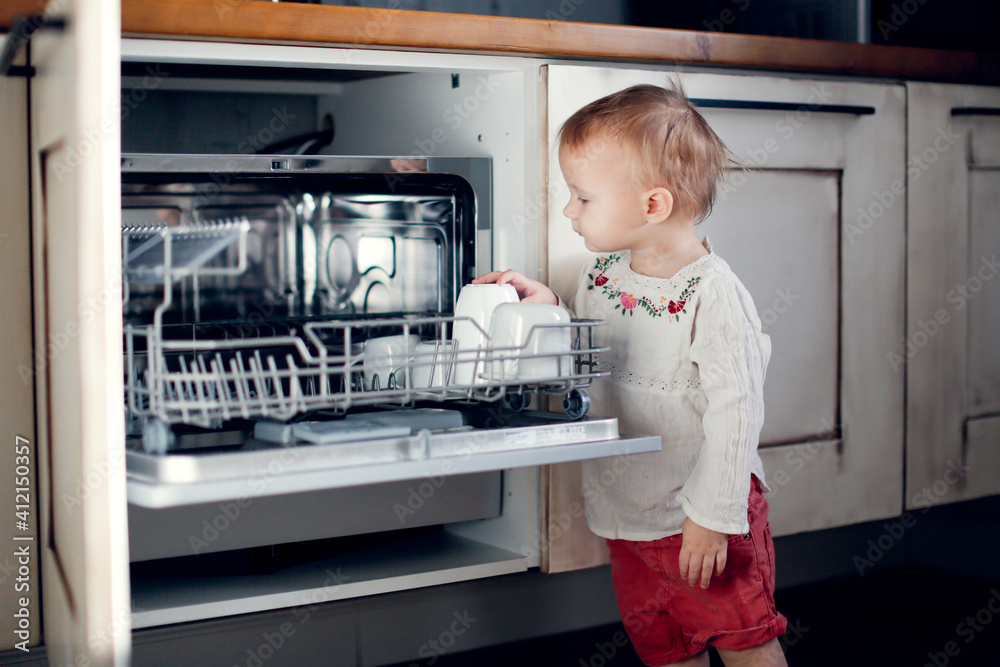 child toddler unloads the dishwasher on his own in a Scandinavian-style kitchen, child's mother's helper, housework with the child, household chores, household child toddler unloads the dishwasher on his own in a Scandinavian-style kitchen, child's mother's helper, housework with the child, household chores, household