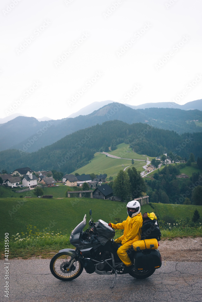 A girl in a yellow raincoat, shoe covers and a motorbike helmet. Motorcyclism and travel. Vertical photo. Top of the Mountains. A day with clouds. Difficult test and extreme vacation. Biker outfit. A girl in a yellow raincoat, shoe covers and a motorbike helmet. Motorcyclism and travel. Vertical photo. Top of the Mountains. A day with clouds. Difficult test and extreme vacation. Biker outfit.