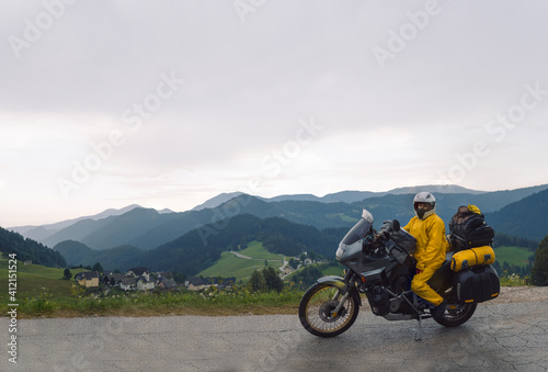 A girl in a yellow raincoat  shoe covers. Motorcyclism and travel. Sightseeing tour. Top of Mountains. A day with clouds. Difficult test and extreme vacation. Biker outfit. High resolution panorama