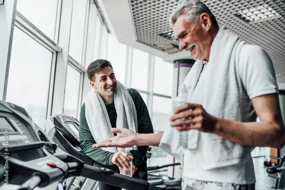 Portrait of two men in the gym, they communicate with each other on treadmills and drink water. Cardio, sports, health Portrait of two men in the gym, they communicate with each other on treadmills and drink water. Cardio, sports, health