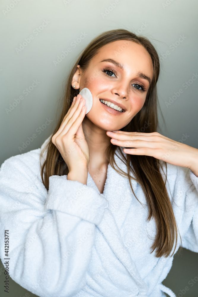 Beautiful woman touching her face with sponge and smiling while standing in front of the mirror Beautiful woman touching her face with sponge and smiling while standing in front of the mirror