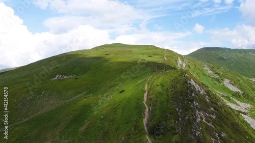 aerial view of green mountains with mountain trails on a background of blue sky
