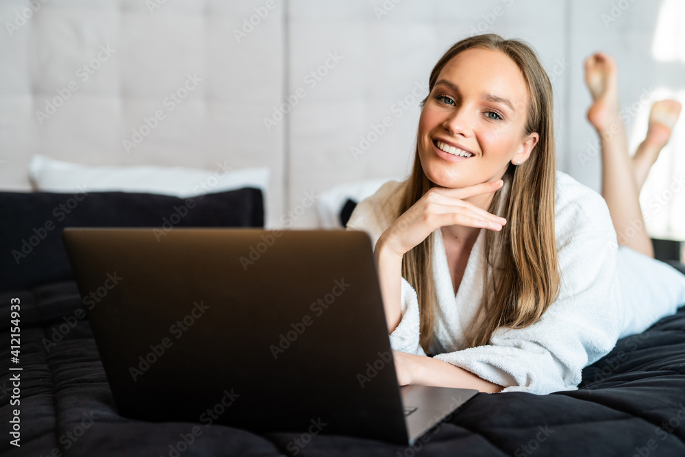 Young woman sitting on bed, working on laptop