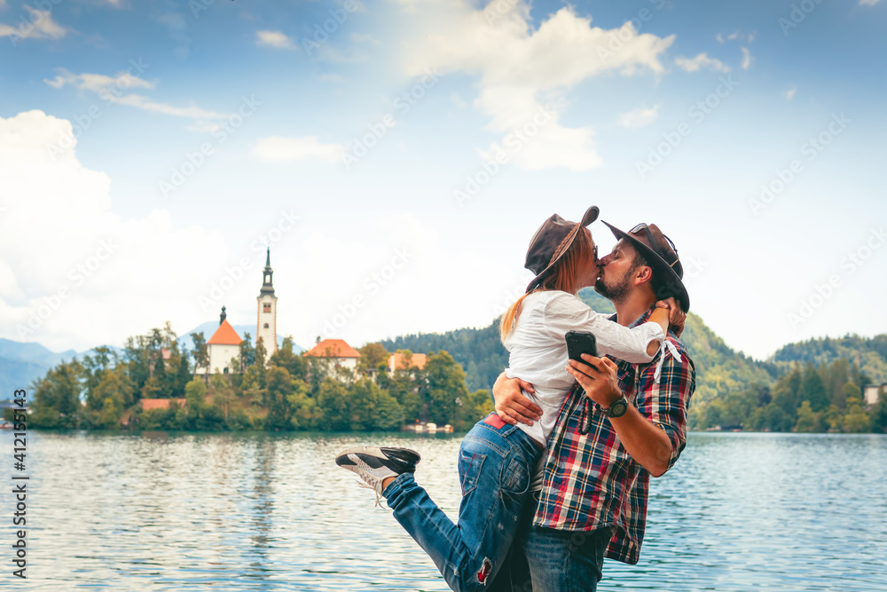 Happy couple of tourists in love is kissing on the background with Bled Lake and Church on the Island, Slovenia. Summer time in Europe. Copy space