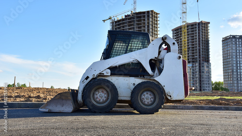 Skid-steer loader for loading and unloading works on city streets. Сompact construction equipment for work in limited conditions. Road repair at construction site. Tower cranes during construction