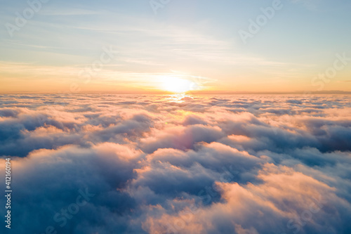 Aerial view of bright yellow sunset over white dense clouds with blue sky overhead.