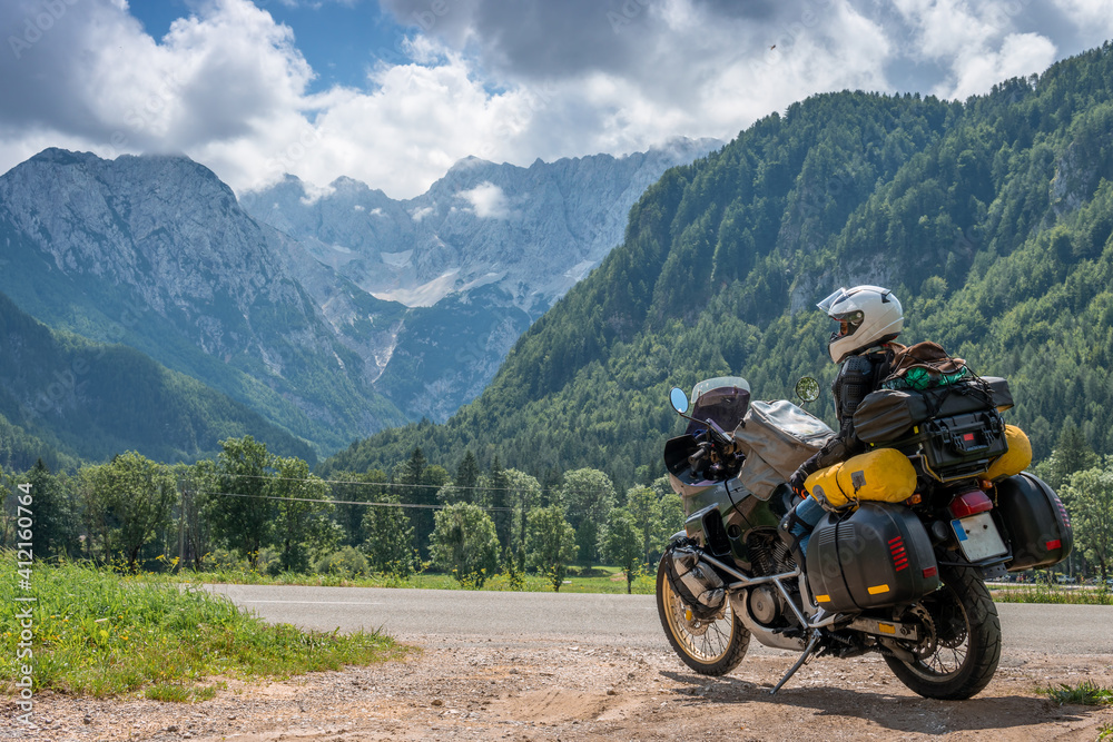 Girl in full body protection, turtle armor, knee pads and helmet, tourer motorcycle for traveling with large luggage, on a background of green mountains, travel and freedom. Zgornje Jezersko Slovenia Girl in full body protection, turtle armor, knee pads and helmet, tourer motorcycle for traveling with large luggage, on a background of green mountains, travel and freedom. Zgornje Jezersko Slovenia